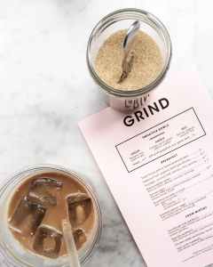 clear drinking glass filled with tea and ice cubes with clear plastic straw beside clear glass canister filled with brown sugar